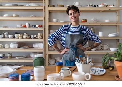 Happy joyful young Turkish woman successful self-employed potter wearing apron behind table with pottery tools smiling at camera, cheerful female ceramist posing against display of handmade ceramics - Powered by Shutterstock