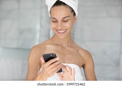 Happy joyful young woman reading text on mobile phone screen after morning shower, using app on cellphone at home, checking messages on social media, chatting online, flirting on dating website