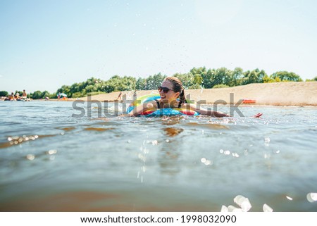 happy, joyful young woman in sunglasses swims on an inflatable circle in river on sunny summer day.. girl is enjoying summer vacation on shore of a lake or river. Active recreation. Dynamic image