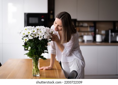 Happy and joyful young woman in white arranging white flowers at home in the kitchen - Powered by Shutterstock