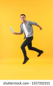 Happy Jumping Asian Programmer With Laptop On Color Background