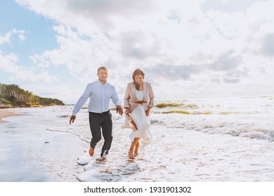 Happy just married middle age couple walk at beach against blue sky with clouds and have fun at summer day. Togetherness, love, family