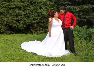 Happy Just Married Multiracial Modern Couple With Piercings, Tattoos, And Dreadlocks Wearing Matching Colors Of Red And Black