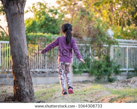 Happy kid, asian baby child girl is walking in the garden, sunset lightl, back side, try to balance body by hand