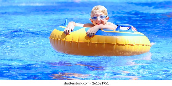 Happy Kid, Blonde Caucasian Boy, Having Fun Floating And Sliding In Waterpark On Inflatable Ring Enjoying Sunny Summer Vacations In Tropical Resort