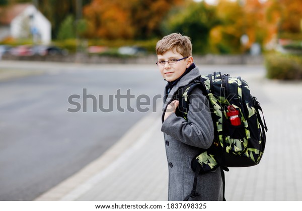 Happy\
kid boy with glasses and backpack or satchel. Schoolkid in stylish\
fashon coan on the way to middle or high school on cold autumn day.\
Healthy child outdoors on the street, on rainy\
day.