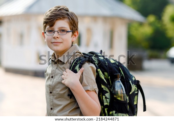 Happy\
kid boy with glasses and backpack or satchel. Schoolkid in on the\
way to elementary or middle school on warm sunny summer day.\
Healthy child outdoors on the street in the city\
.