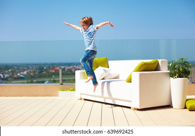 Happy Kid, Boy Jumping From The Couch On Roof Top Terrace At Warm Sunny Day