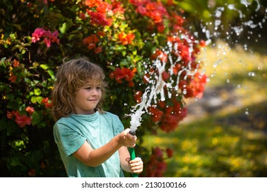 Happy Kid Boy Pours Water From A Hose. American Kids Childhood. Child Watering Flowers In Garden. Home Gardening.