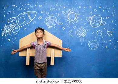 happy kid with cardboard rocket on back with space, universe and planets doodle drawing on wall - concept showing of childhood dream about astronaut or scientist