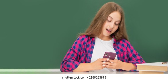 Happy Kid Chatting On Smartphone In Classroom At Blackboard, Message. Horizontal Isolated Poster Of School Girl Student. Banner Header Portrait Of Schoolgirl Copy Space.