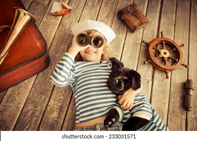 Happy Kid Dressed In Sailor. Child Playing With Dog. Baby Having Fun At Home. Travel And Adventure Concept. Unusual High Angle View Portrait