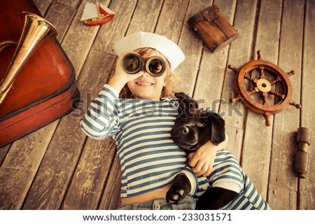 Happy kid dressed in sailor. Child playing with dog. Baby having fun at home. Travel and adventure concept. Unusual high angle view portrait