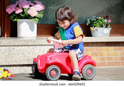 Happy Kid Driving A Toy Car With Hause Background.