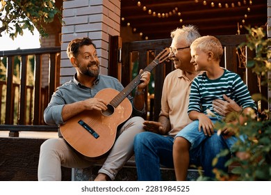 Happy kid enjoying with his father and grandfather in the backyard. Focus is on father playing acoustic guitar. - Powered by Shutterstock