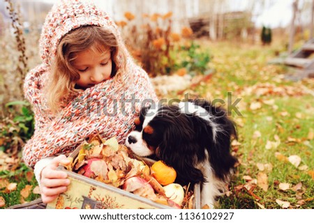 Foto Bild fröhliches Kind Mädchen mit einem Korb voller Äpfel, das mit ihrem Hund spielt.