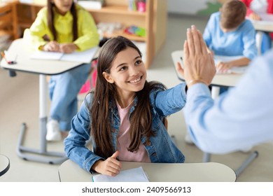 Happy kid girl giving high five to female teacher in classroom. Teacher encouraging helping child student giving support during elementary junior school lesson - Powered by Shutterstock