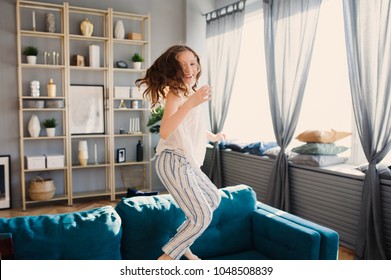 Happy Kid Girl Playing At Home In Weekend Morning And Jumping On Couch In Modern Scandinavian Interior