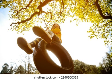 Happy kid girl playing outdoors in the garden. Child swing on rubber tire from car wheel. Green future. Sustain.  - Powered by Shutterstock