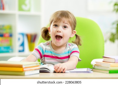 Happy Kid Girl Reading Book At Table In Nursery