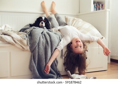 Happy Kid Girl Waking Up In The Morning In Her Bedroom With Dog In Bed