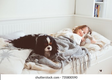 Happy Kid Girl Waking Up In The Morning In Her Bedroom With Dog In Bed