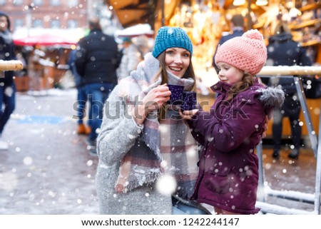 Happy kid girl and young beautiful woman with cup of steaming hot chocolate and mulled wine. Adorable child and beautiful mum on Christmas market in Germany. Family walking on Xmas market.