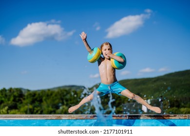 Happy kid having fun when jumping to swimming pool with inflatable armbands. Summer outdoor water activity for kids. - Powered by Shutterstock