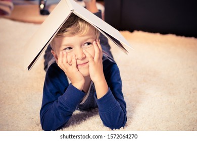 Happy kid having fun while lying down on carpet with book on his head. 