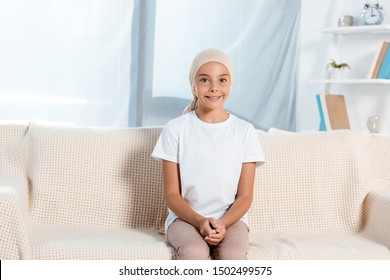 Happy Kid In Head Scarf Sitting On Sofa In Living Room 