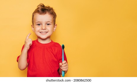 The happy kid is holding a toothbrush on a yellow background and smiling showing his teeth. Health care, oral hygiene. A place for your text. - Powered by Shutterstock