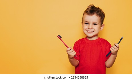 The happy kid holds 2 toothbrushes on a yellow background in both hands and smiles showing his teeth. Health care, oral hygiene. A place for your text. - Shutterstock ID 2234358885