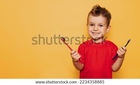 The happy kid holds 2 toothbrushes on a yellow background in both hands and smiles showing his teeth. Health care, oral hygiene. A place for your text.