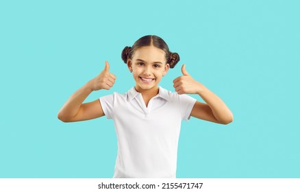 Happy Kid. Joyful Child In Cotton Tennis Tee Says Well Done, Yes, Okay, Excellent, Perfect. Girl In Polo Tshirt, With Cute Hair Buns Standing Isolated On Blue Looks At Camera, Smiles, Gives Thumbs Up