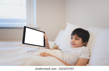 Happy Kid Lying In Bed Holding Tablet Watching Cartoon And Chatting With Friends On Digital Pad, Cute Young Boy Showing Touch Pad, Child Relaxing In The Morning Before Go To School