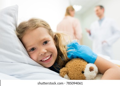 Happy Kid Lying On Hospital Bed While Mother Talking With Doctor