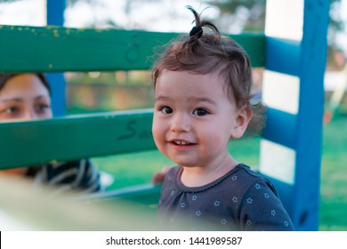 Happy Kid On Kids Playground Playing Hide And Go Seek With Mom. Laughing Child Plays Peek A Boo With Mother Outdoors In Nature. Smiling Toddler And Woman Play Games On Sunny Day. Adult Spying On Baby.