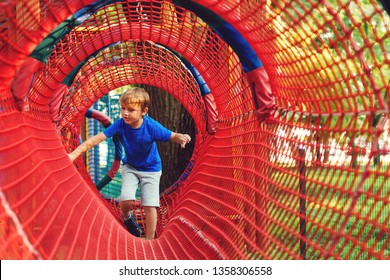 Happy kid overcomes obstacles in rope adventure park. Summer holidays concept. Little boy playing at rope adventure park. Modern amusement park for kids. Outdoors games - Powered by Shutterstock