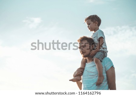 Happy kid playing with father. Dad and son outdoors. Father carrying child on his back. Happy family in summer field. 