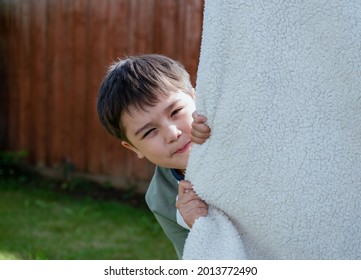 Happy kid playing hide and seek in the garden, Cute boy looking at camera with smiling face while standing behind blanket hanging on clothesline, Funny child playing outdoor on sunny day summer.
