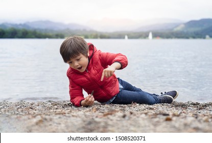 Happy kid playing pebbles and leaves with blurry nature background, Chid lyingdown on pebbles by the lake playing alone in sunny day, little boy playing outdoor in spring or summer
