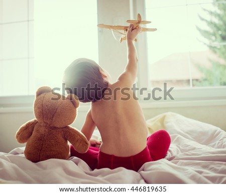 Happy kid playing with wooden toy airplane and Teddy bear in bedroom