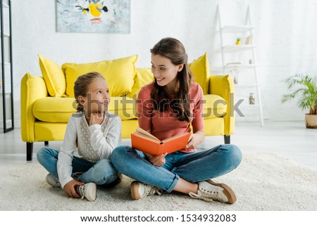 happy kid sitting on carpet with babysitter holding book 
