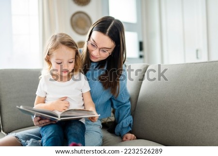 A happy kid sitting on sofa with babysitter holding book