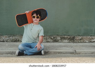 Happy Kid With Skateboard And Sunglasses Sitting On The Street