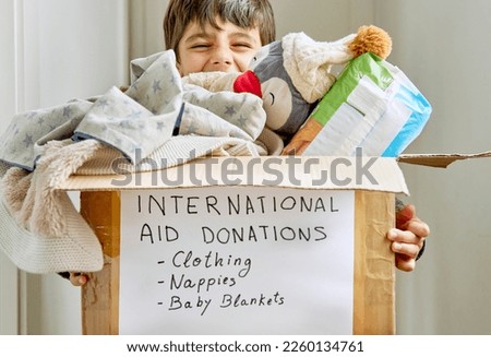 Happy kid supporting a box with humanitarian aid for a natural disaster victims. Kid donates his old clothes and toys for other children who are suffering from natural disaster.
