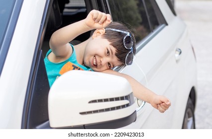 Happy Kid In White Car Looking In Rear View Retractable Lateral Mirror Through Lateral Door Window.joyful Child Boy Ready Fir Trip Travel By Car.family Adventure Smiling Kid Hands Up Expressing Hooray