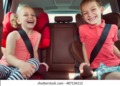 Happy Kids, Adorable Girl With Her Brother Sitting Together In Modern Car Locked With Safety Belts Enjoying Family Vacation Trip On Summer Weekend