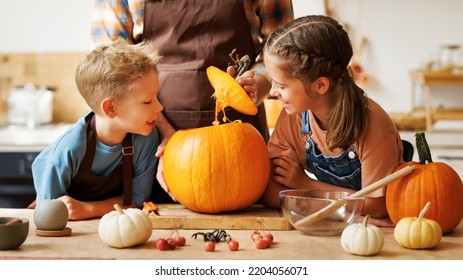 Happy kids boy and girl helping father to carve Halloween pumpkin while standing in kitchen at home and preparing for autumn holiday, family children and dad making Jack-o-Lantern together - Shutterstock ID 2204056071