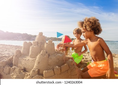 Happy kids decorating sandcastle towers with flags